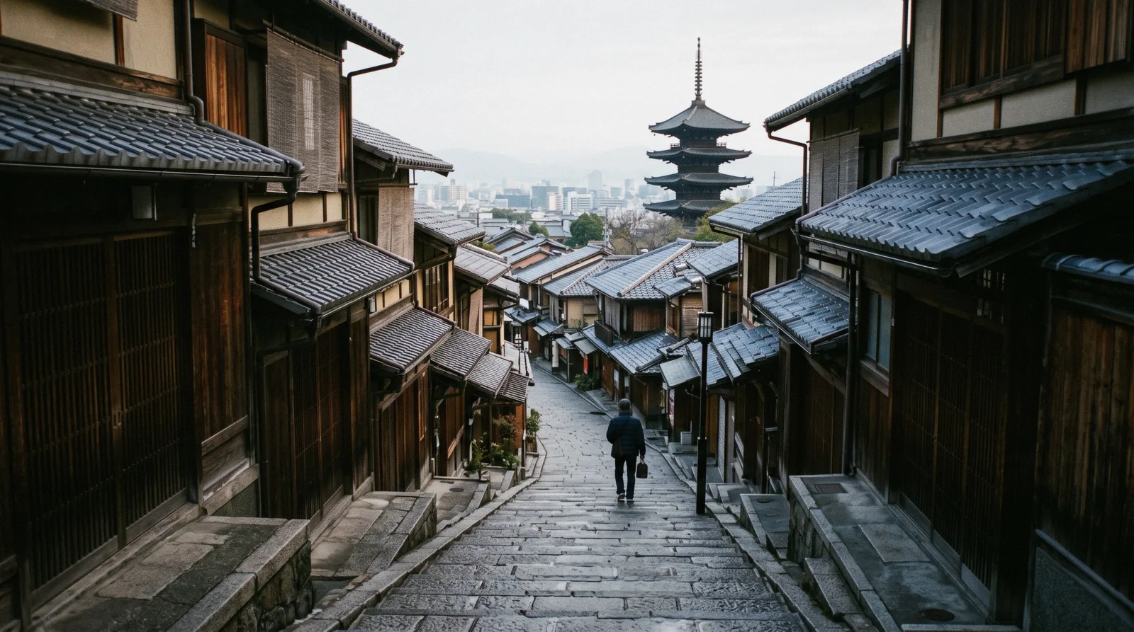 Tiled machiya rooftops falling away towards the city from a sloping lane, Kyoto neighborhoods Japan