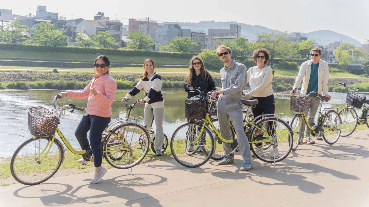 Cyclists on e-bikes beside a temple gate on a morning Kyoto e-bike tour, Kyoto Japan